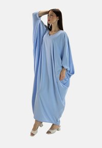 Robe surdimensionnée de couleur bleu clair en matériau doux, avec des manches longues et larges, un col en V et des poches latérales, assortie à des talons blancs.