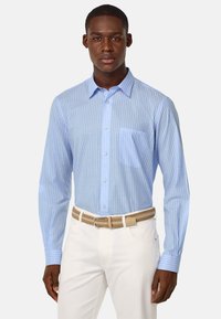 Chemise boutonnée rayée bleu clair avec une poche poitrine unique, manches longues, en tissu lisse, portée avec un pantalon crème et une ceinture tressée.