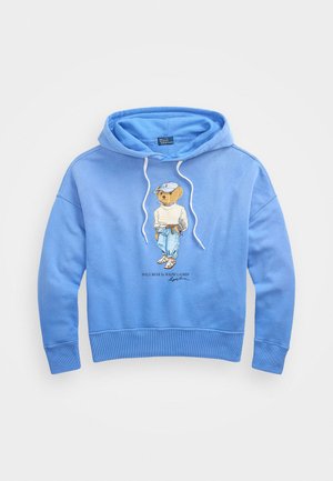 Gaiši zils kokvilnas kapucis ar auklu. Uz tā ir izšūts karikatūras lācis polo tērpā, un tam ir ribotas piedurknes un apakšmala.