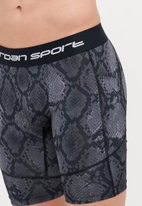 Fekete és szürke kígyóbőrmintás sportnadrág széles elasztikus derékkal, amelyen a "Jordan Sport" felirat látható, valamint oldalsó zsebbel.