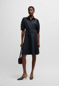 Navy shirt dress made of smooth fabric, featuring short sleeves, a button front, cinched waist with a belt, and a flared skirt.
