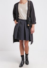 Svart kavaj över en metallisk silvertopp, tillsammans med en strukturerad kolgrå kjol och svarta ankelstövlar. En liten svart väska med kedjestropp.