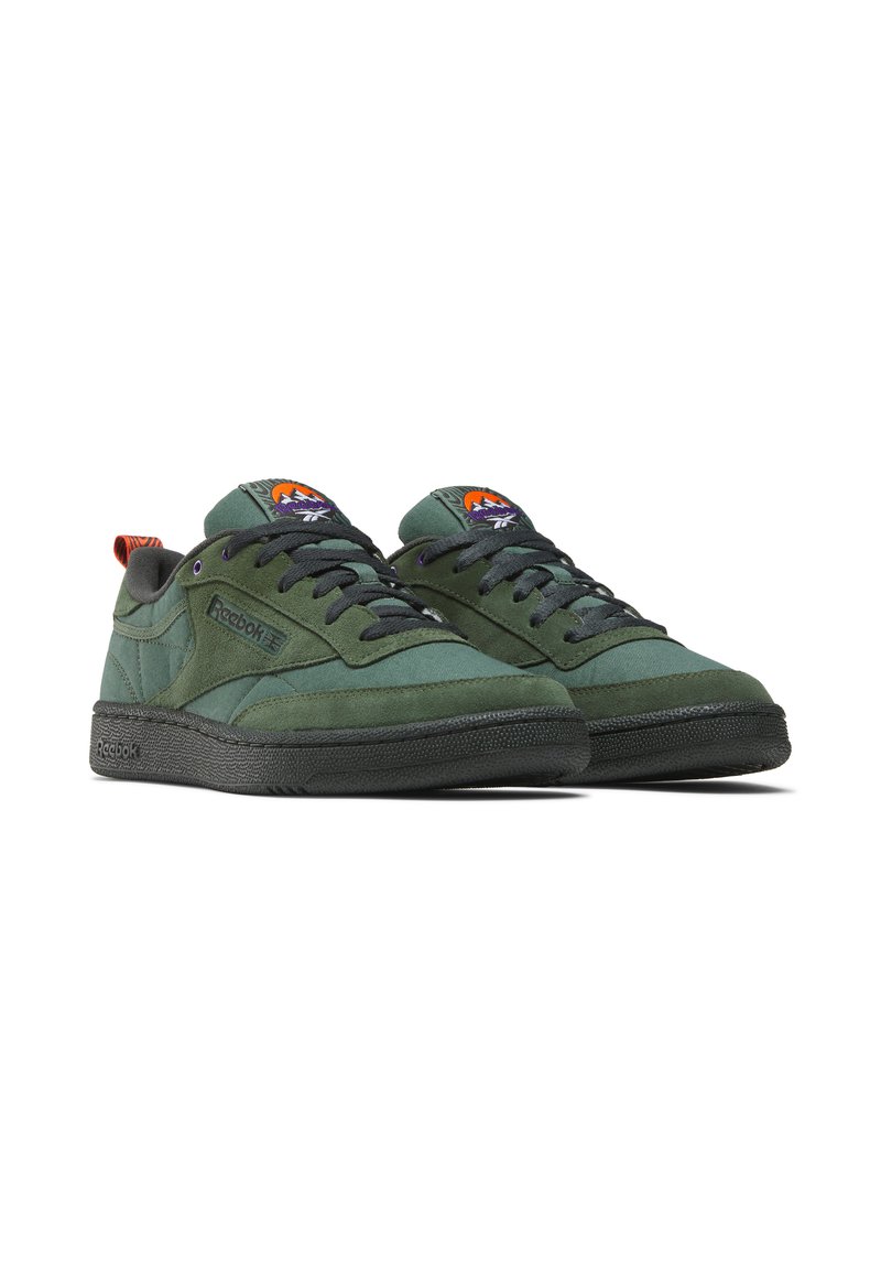 Baskets en suède vert avec semelles en caoutchouc noir, dotées d'un col rembourré, d'un bout rond et d'accents contrastants orange et violet sur la languette.