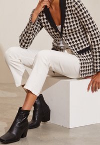 Houndstooth patterned blazer in black and cream with a black collar, paired with white cropped pants and black leather ankle boots.