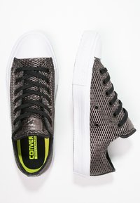 Baskets en mesh noir avec embout et semelle en caoutchouc blanc, dotées de lacets, œillets noirs et d'un détail de semelle intérieure vert citron vif.