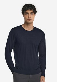 Marinblå stickad tröja med långa ärmar, ribbad halsringning och nederkant, slät textur, figurnära design och subtil sömnadsdetalj vid axlarna.