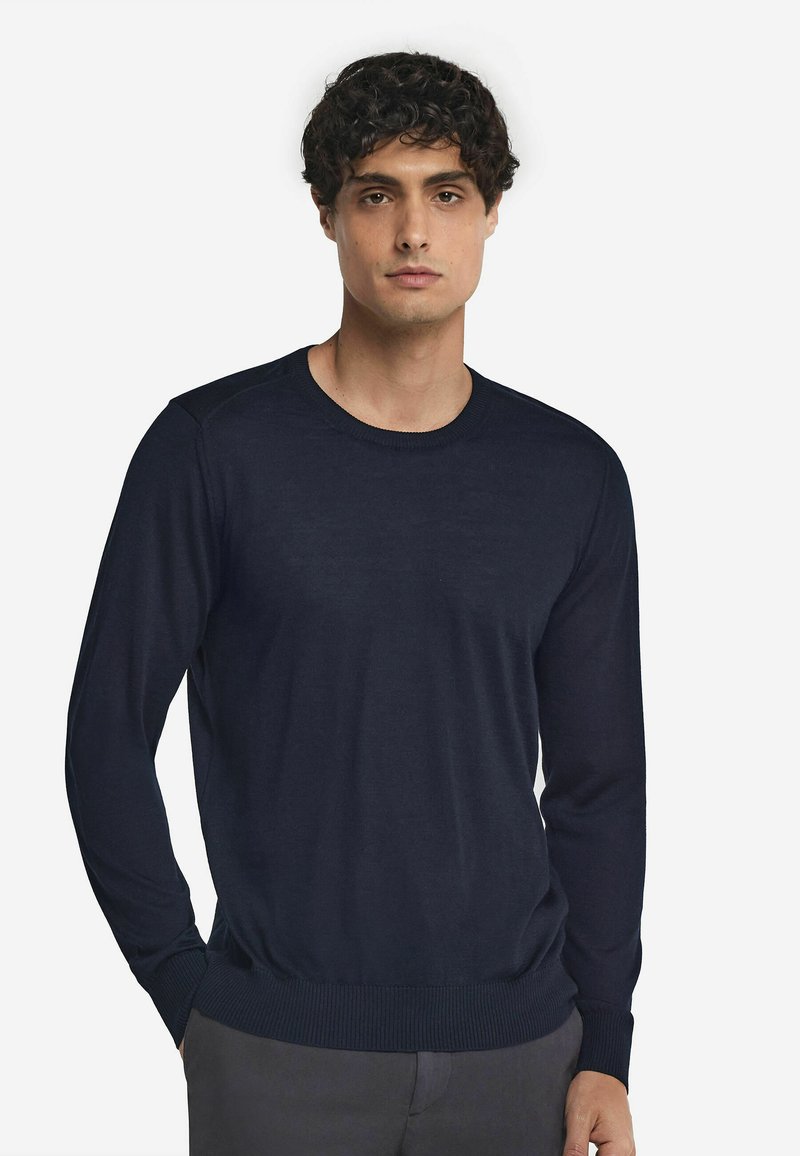 Marinblå stickad tröja med långa ärmar, ribbad halsringning och nederkant, slät textur, figurnära design och subtil sömnadsdetalj vid axlarna.