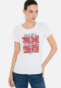 T-shirt bianca in cotone con una grafica di labbra rosse in un motivo a griglia. Maniche corte, scollo rotondo e logo nella parte inferiore.