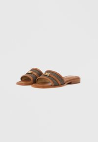 Brune slide-sandaler med to mørke stribede stofbånd, med en guldfarvet logoaccent og en flad tan sål, lavet af blødt læder.