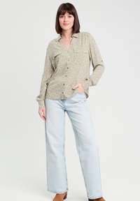 Long-sleeve patterned blouse in light green and cream with button closure and two front pockets, paired with light blue wide-leg jeans.