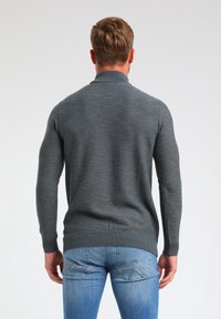 Harmaa neulepaita, jossa on ribbikaarroke ja helma, sekä tekstitetty kuvio. Yhdistettynä sinisiin farkkuihin. Katsottu takaa.