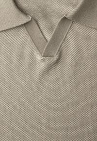 Primo piano di tessuto beige lavorato a maglia con scollo a V e trama a coste su un maglione o una polo.