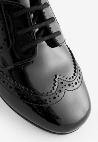 Zwarte lakschoenen met een ronde neus, voorzien van brogue-details, perforaties en stevige zwarte veters. Gladde, glanzende textuur.