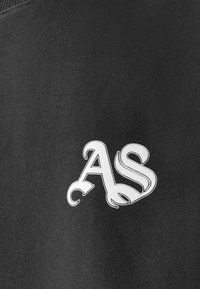 Tessuto nero con un logo ricamato bianco ben visibile "AS" e decorazioni floreali. La trama sembra liscia e morbida.
