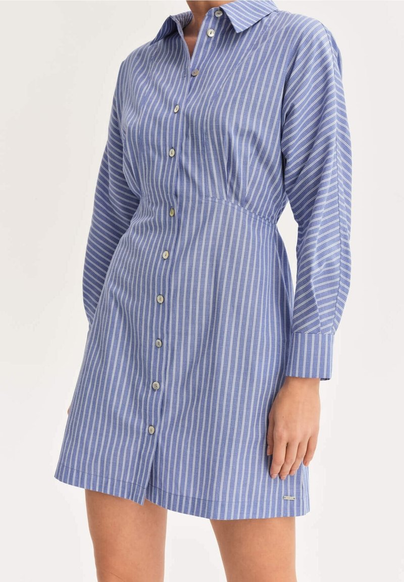 Robe chemise à rayures bleues et blanches avec manches longues, boutonnée à l'avant et col. Dotée d'une taille élastiquée et de poches latérales. Tissu à texture lisse.