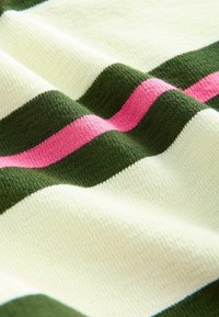 Nærbillede af tekstureret stof med skiftevis brede creme- og grønne striber samt en smal pink stribe, der løber horisontalt.