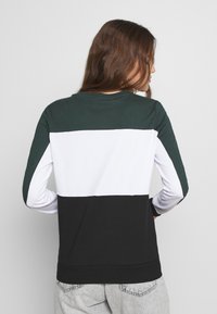 Långärmad tröja i mörkgrön, vit och svart färgblock; har rund halsringning och mjuk bomullstextur.