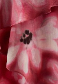 Tissu rose et blanc à volants avec un motif d'empreintes de pattes noires sur un matériau texturé et léger.