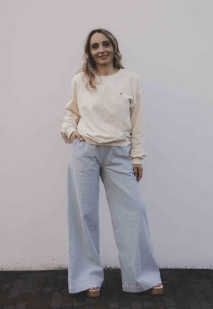 Crème sweatshirt met een klein roze logo, gecombineerd met wijde gestreepte broeken in lichtblauw en wit. Model draagt tan platform schoenen.