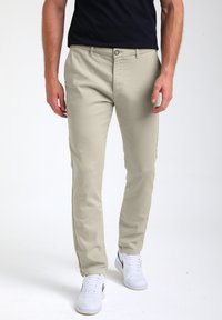 Chino in cotone beige con design slim fit, dotati di chiusura con bottone frontale, tasche laterali e abbinati a sneakers bianche.