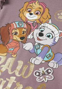 Fioletowa koszulka z rysunkowymi psami w różnych kolorach i strojach. Złoty brokatowy napis "Paw Patrol" oraz naszywka w kształcie motyla.