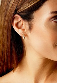 Goldfarbene Ohrringe mit gestapeltem Design, die glatte, runde Formen aufweisen. Die Oberfläche hat ein poliertes Finish. Tragen an einem Ohr einer Person.