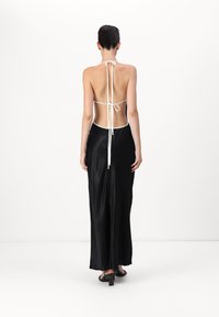 Back view of a black satin dress with a low back, white tie straps, and a flowing silhouette. Features a smooth, glossy texture.
