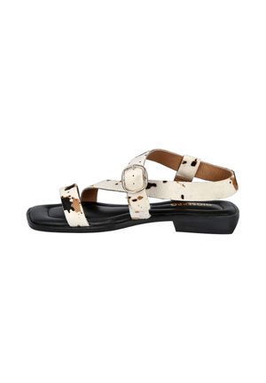 Sandalia plana blanca con tiras estampadas de vaca en negro y marrón, hebilla plateada y suela acolchada negra.