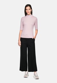Pink fitted turtleneck top with short sleeves, paired with black wide-leg trousers. Casual sneakers with light accents complete the outfit.
