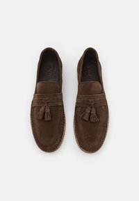 Mocassini in suede marrone con dettagli a frange, caratterizzati da una punta arrotondata cucita e una suola in gomma flessibile. Texture liscia con un design classico.