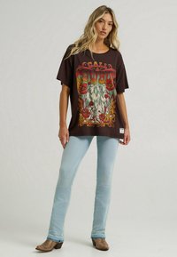 Czarny, oversize t-shirt z kolorową grafiką koni i kwiatów. Noszony z jasnoniebieskimi dżinsami i brązowymi butami za kostkę w wzory.