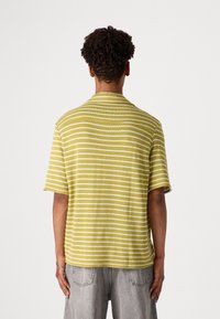 Chemise à manches courtes jaune avec des rayures blanches, fabriquée en tissu texturé. Présente un col ouvert et une coupe décontractée. Vue de dos affichée.
