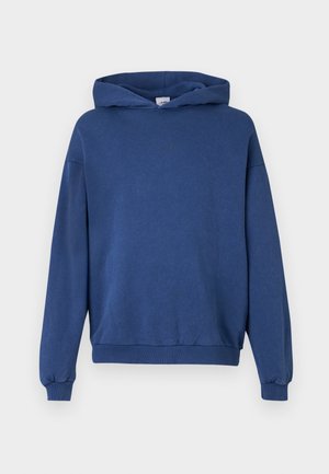 Zila kapuce, kas izgatavota no mīksta auduma, ar kangaru kabatu, garām piedurknēm un ribotām aprocēm. Diskrēta logo uz krūtīm.