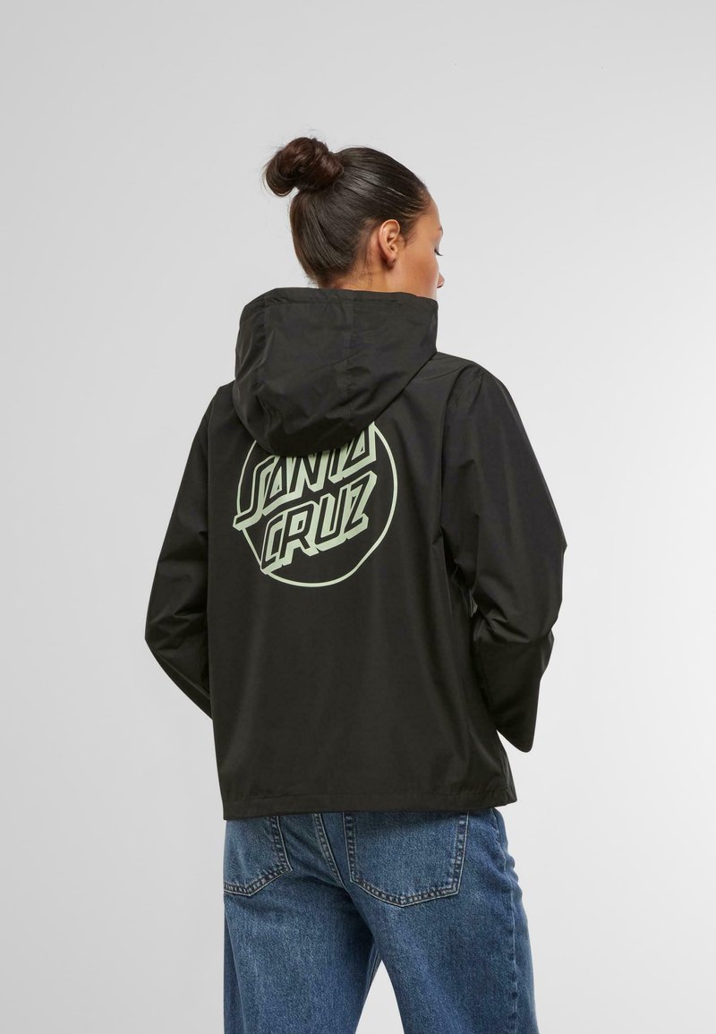 Black jacket with a hood, featuring a large mint green "SANTA CRUZ" logo on the back. Smooth texture and casual fit, worn with blue jeans.