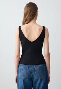 Czarny prążkowany top na ramiączkach z głębokim dekoltem z tyłu, połączony ze średnio niebieskimi dżinsami z klasycznym pięciopunktowym fasonem i prostymi nogawkami.
