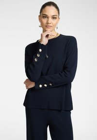 Maglione lavorato a maglia blu navy con maniche lunghe, caratterizzato da bottoni dorati sui polsini e un leggero design a orlo sceso.