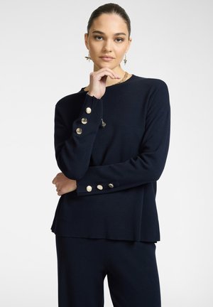 Maglione lavorato a maglia blu navy con maniche lunghe, caratterizzato da bottoni dorati sui polsini e un leggero design a orlo sceso.