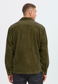 Chemise en velours côtelé vert avec une finition texturée, manches à boutons et coupe décontractée, vue de dos sur fond clair.