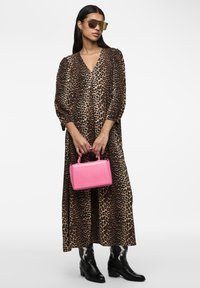 Maxi dress con stampa leopardata e maniche ampie, abbinato a una piccola borsa a tracolla in pelle stampata coccodrillo rosa e stivali cowboy neri.