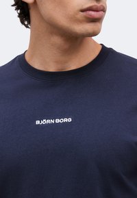 Jeune personne portant un t-shirt bleu marine à col rond avec le logo blanc Björn Borg centré sur la poitrine.