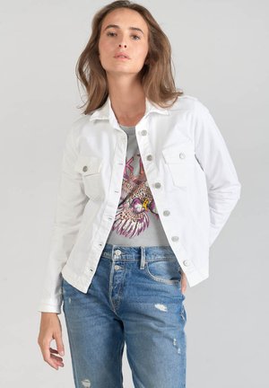 Witte denimjas met knoopsluiting, twee borstzakken en een iets getailleerd ontwerp, gedragen over een graphic t-shirt en versleten blauwe jeans.
