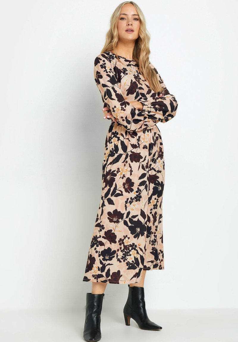 Blumiges langärmeliges Kleid in sanftem Rosa mit dunklen Blumenmustern, tailliertem Bund und fließendem Rock; kombiniert mit schwarzen Knöchelstiefeln.