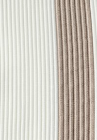 Textile présentant des motifs verticaux en côtes alternées en blanc cassé et en nuances de brun clair, mettant en valeur une texture douce et un contraste de couleurs subtil.