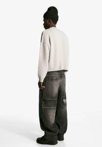 Sivé voľné džínsy s viacerými vreckami a bielym prešívaním, doplnené o svetlo sivý voľný sveter a čierny pletený klobúk.