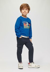 Niebieska bluza z grafiką, ciemne spodnie cargo i wielokolorowe sneakersy. Gładki materiał, luźny krój i elastyczne mankiety w spodniach.