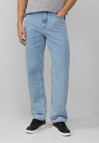 Jeans en denim bleu clair avec une coupe droite, dotés de poches standard et d'une taille classique, associés à des chaussures de sport noires.