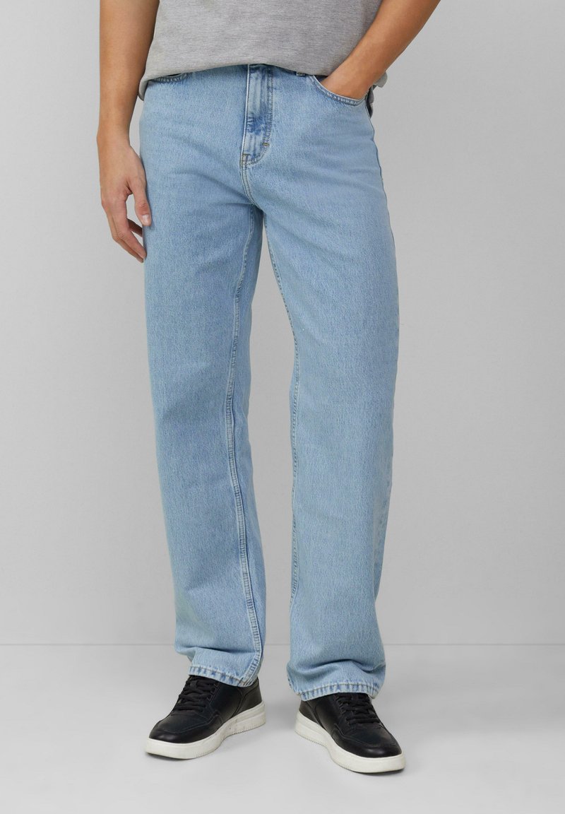 Jeans en denim bleu clair avec une coupe droite, dotés de poches standard et d'une taille classique, associés à des chaussures de sport noires.