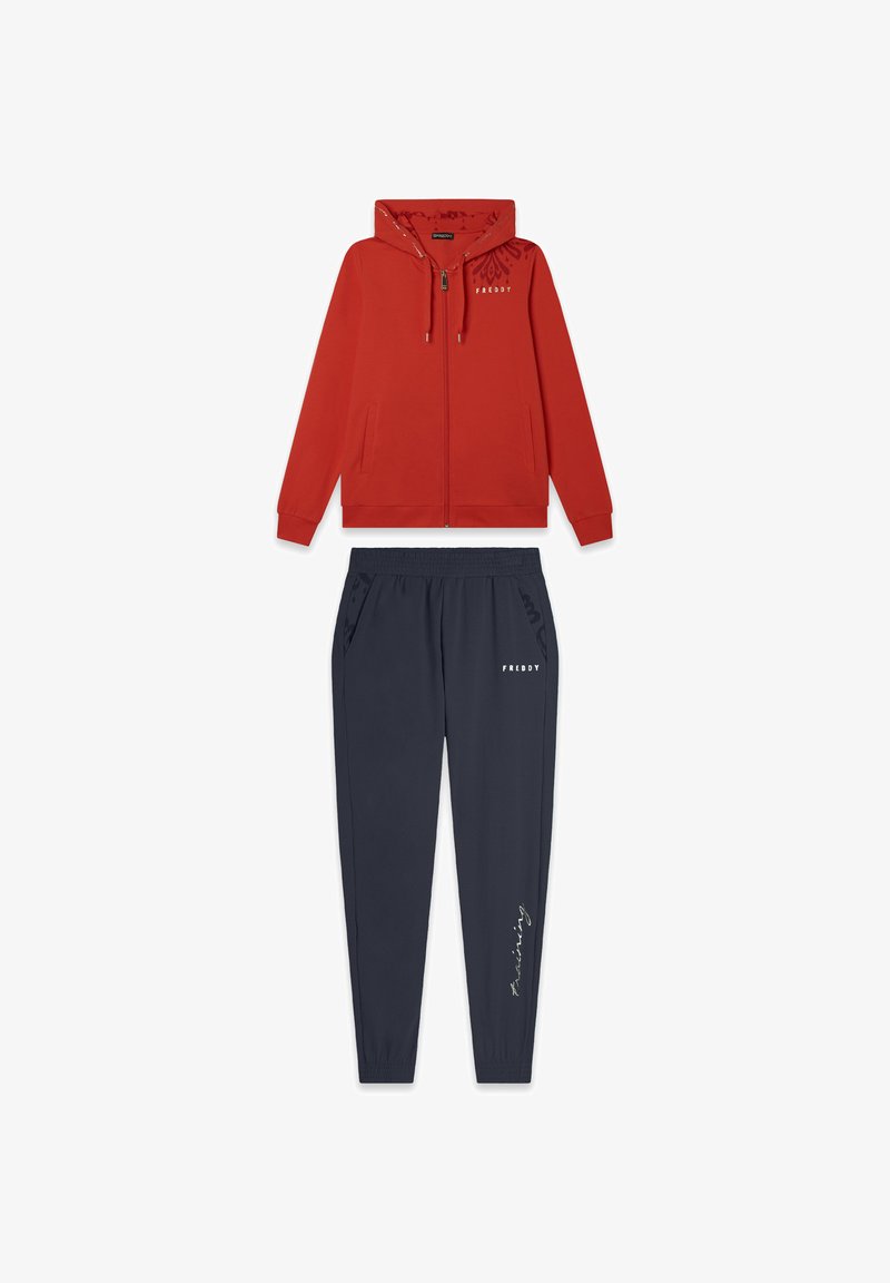 Sudadera roja con cremallera y capucha, con bolsillos laterales, combinada con pantalones jogger marinos con cintura elástica y un detalle de texto estampado.