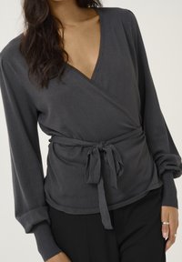 Grau wickelndes Oberteil aus weichem Stoff, mit tiefem V-Ausschnitt, langen Ärmeln mit eng anliegenden Bündchen und einem gebundenen Taillendetail für eine verstellbare Passform.