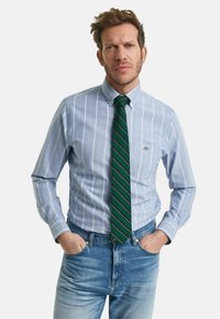 Lyseblå skjorte med hvide striber, parret med et grønt slips med gule striber. Båret med slidte blå jeans.